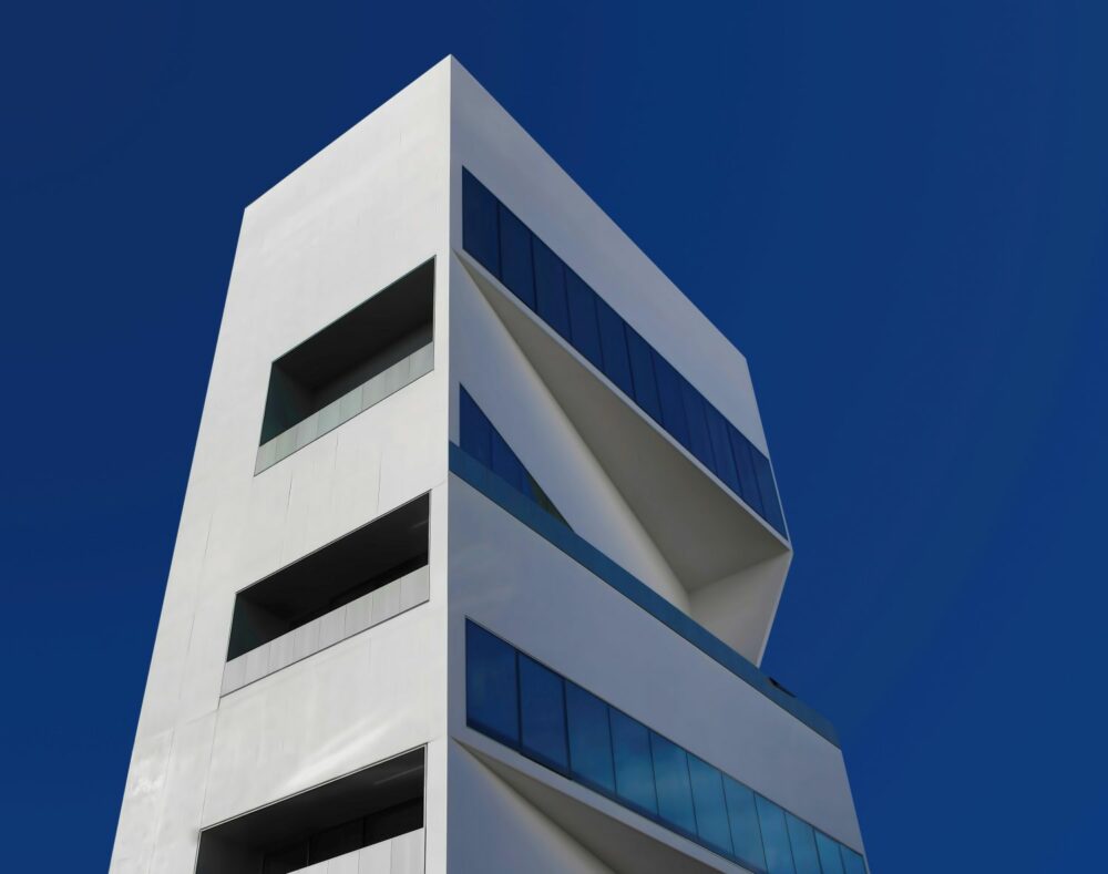 Contemporary white tower with sharp geometric lines and blue glass panels, reflecting luxury branding, lifestyle marketing, and innovative design.