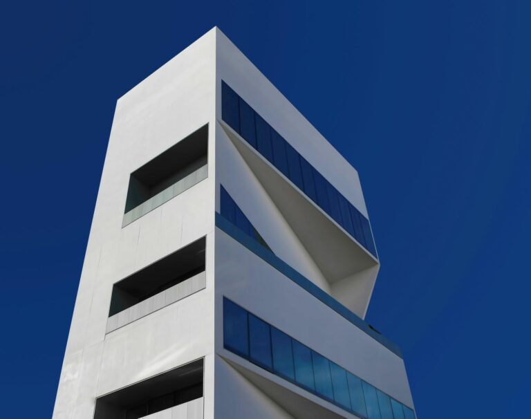 Contemporary white tower with sharp geometric lines and blue glass panels, reflecting luxury branding, lifestyle marketing, and innovative design.
